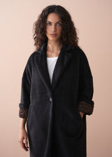 Woman wearing a dark coat with leopard cuffs on a beige background