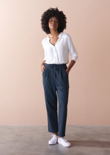 Woman wearing a white blouse and dark grey jersey trousers against a beige background