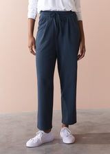 Person wearing dark grey jersey trousers with a white shirt and white sneakers on a beige background