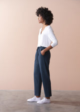 Person wearing a white shirt and dark grey jersey trousers against a beige background