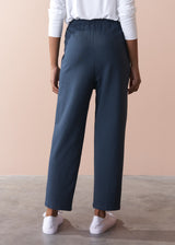 Person wearing dark grey jersey trousers and white shoes on a beige background