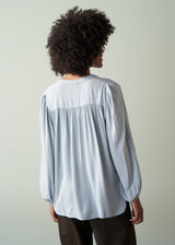 Woman wearing a light blue shirt and dark green trousers with a plain background