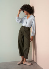 Woman wearing a light blue shirt and dark green trousers with a plain background