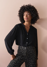 Woman wearing a black blouse and leopard print trousers against a beige background