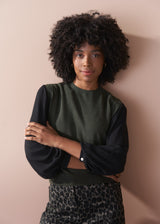 Woman wearing a dark green sweater and leopard print trousers against a beige background
