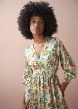 Close-up of a woman in a long, floral, v-neck satin dress, against a beige wall.