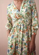 Close-up of shearing detail on a long, floral, v-neck satin dress, against a beige wall.