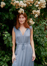 Woman in a light blue dress standing in front of green foliage and white flowers