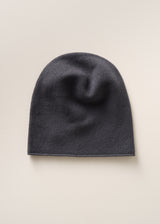 A dark charcoal gray knit beanie hat, shown flat against a light beige background.