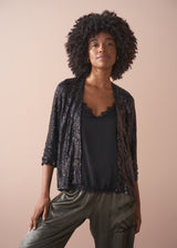 Woman wearing a black sequin jacket, black satin camisole and green satin trousers against a beige background