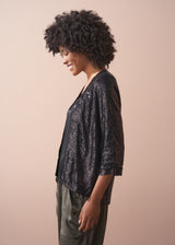 Woman wearing a black sequin jacket, black satin camisole and green satin trousers against a beige background