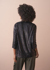 Woman wearing a black sequin jacket, black satin camisole and green satin trousers against a beige background