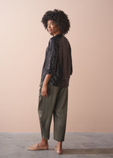 Woman wearing a black sequin jacket, black satin camisole and green satin trousers against a beige background