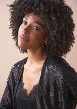 Woman wearing a black sequin jacket against a beige background