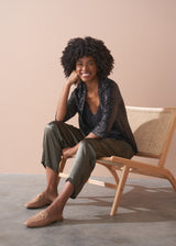 Woman wearing a black sequin jacket, black satin camisole and green satin trousers against a beige background