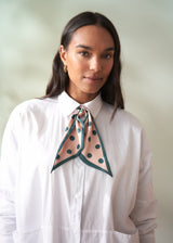 Woman wearing a white shirt with a green polka dot scarf around her neck against a plain background