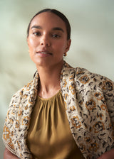 Woman wearing a patterned jacket over a mustard top against a light background