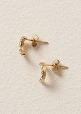 Gold moon stud earrings with embedded crystals on a beige textured background