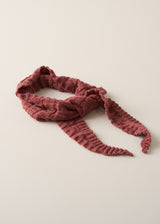 A dusty rose pink chunky knit scarf with a textured cable pattern and fringed ends, tied in a knot and displayed on a light beige background.