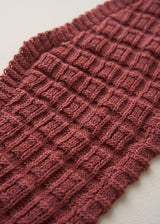 A close-up of a textured knit fabric in a muted dusty rose or mauve color, showing the detailed ribbed and basketweave stitch pattern against a light neutral background.