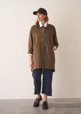 Woman wearing a khaki brown short trench coat over a white shirt on a plain background