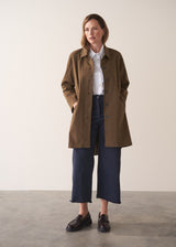 Woman wearing a khaki brown short trench coat over a white shirt on a plain background