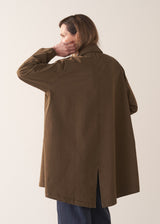 Woman wearing a khaki brown short trench coat over a white shirt on a plain background