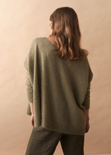 Person wearing a khaki green wool blend sweater against a beige background