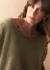 Woman wearing a khaki green wool blend sweater against a beige background