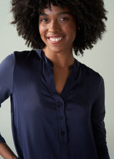 Woman wearing a long, v-neck dark navy satin dress against a plain background