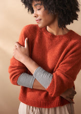 Woman wearing a red sweater with striped sleeves against a beige background