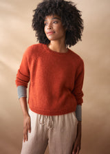 Woman wearing a red sweater and beige pants against a beige background