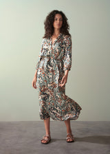 Woman in an abstract print satin midi dress with detachable belt, standing against a green wall