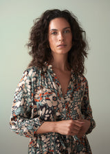 Woman in an abstract print satin midi dress with detachable belt, standing against a green wall
