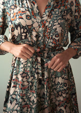 Woman's hands tying a knot in the belt of an abstract print satin midi dress, against a green background