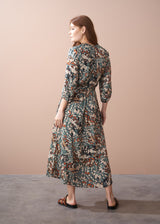Back of woman in an abstract print satin midi dress with detachable belt, standing against a beige wall