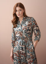 Woman in an abstract print satin midi dress with detachable belt, standing against a beige wall