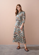 Woman in an abstract print satin midi dress with detachable belt, standing against a beige wall