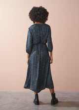 Person wearing a patterned dress standing against a beige wall.