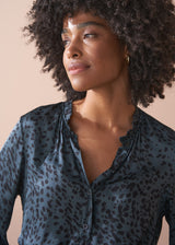 Woman wearing a dark blue satin shirt with a leopard print pattern against a beige background
