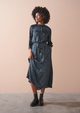 Woman wearing a patterned dress standing against a beige wall.