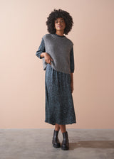 Woman wearing a gray sweater over a patterned dress against a beige background