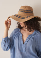 Model wearing an oversized natural straw hat with a blue cotton top, against a beige background