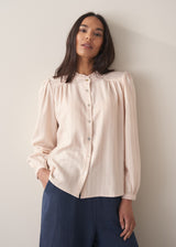 Woman wearing a light pink blouse with pinstripes and long sleeves with dark navy trousers