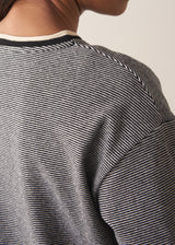 Woman wearing a grey stripe sweater and white jeans against a plain background