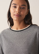 Woman wearing a grey stripe sweater and white jeans against a plain background