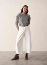 Woman wearing a grey stripe sweater and white jeans against a plain background