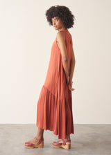 Woman wearing dark orange satin tiered floaty summer dress against a plain background