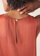 Woman wearing dark orange satin tiered floaty summer dress against a plain background