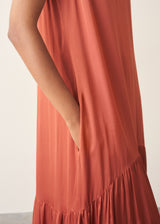 Woman wearing dark orange satin tiered floaty summer dress against a plain background
